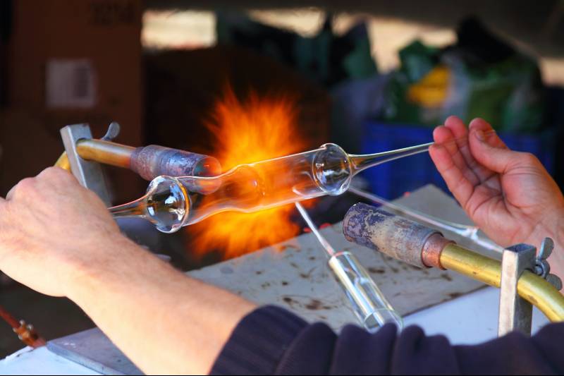 hands holding a blown glass cylinder against a blowtorch