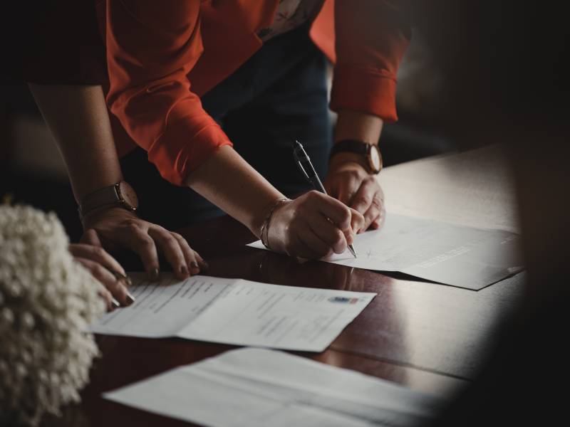 2 people leaning over a desk about to sign papers