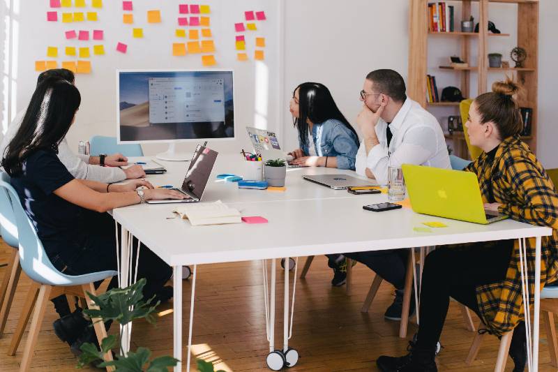 four people around a desk looking at a computer screen